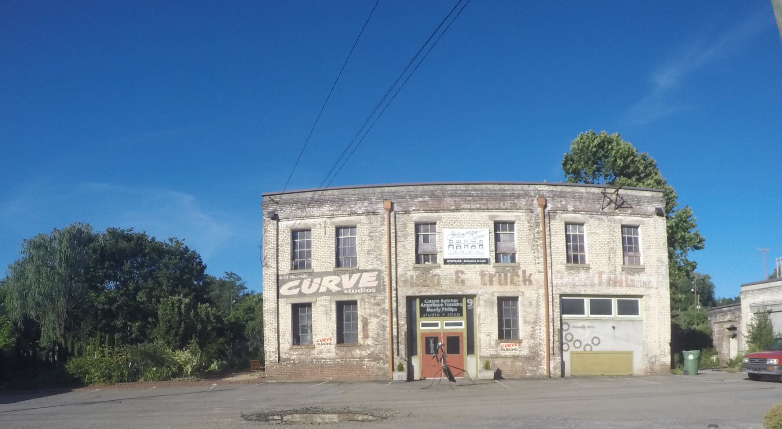 The curved white-brick Curve Studios building on Riverside Drive in Asheville's River Arts District, its painted CURVE studios sign above an empty lot